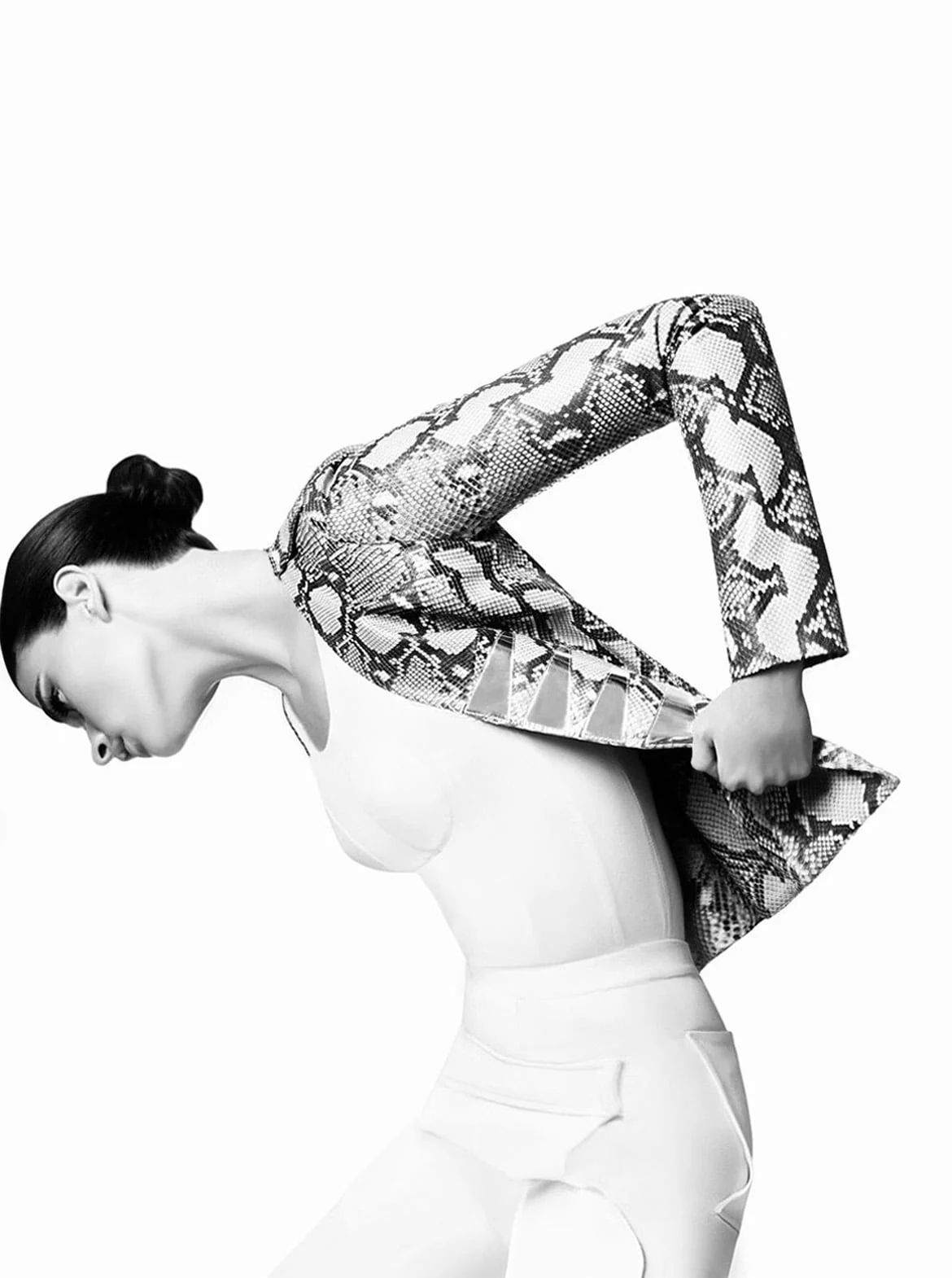 Black and white shot of a model with a slicked bun bending forward, pulling off a python print jacket over white. Photographed by Cameron Krone.