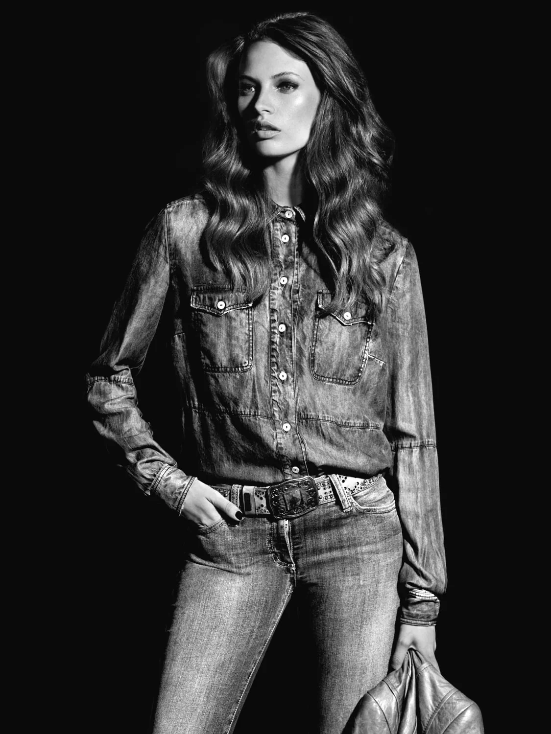 Black and white shot of a model with long wavy hair in a denim western shirt, jeans and buckled belt, for Marie Claire. Photographed by Cameron Krone.