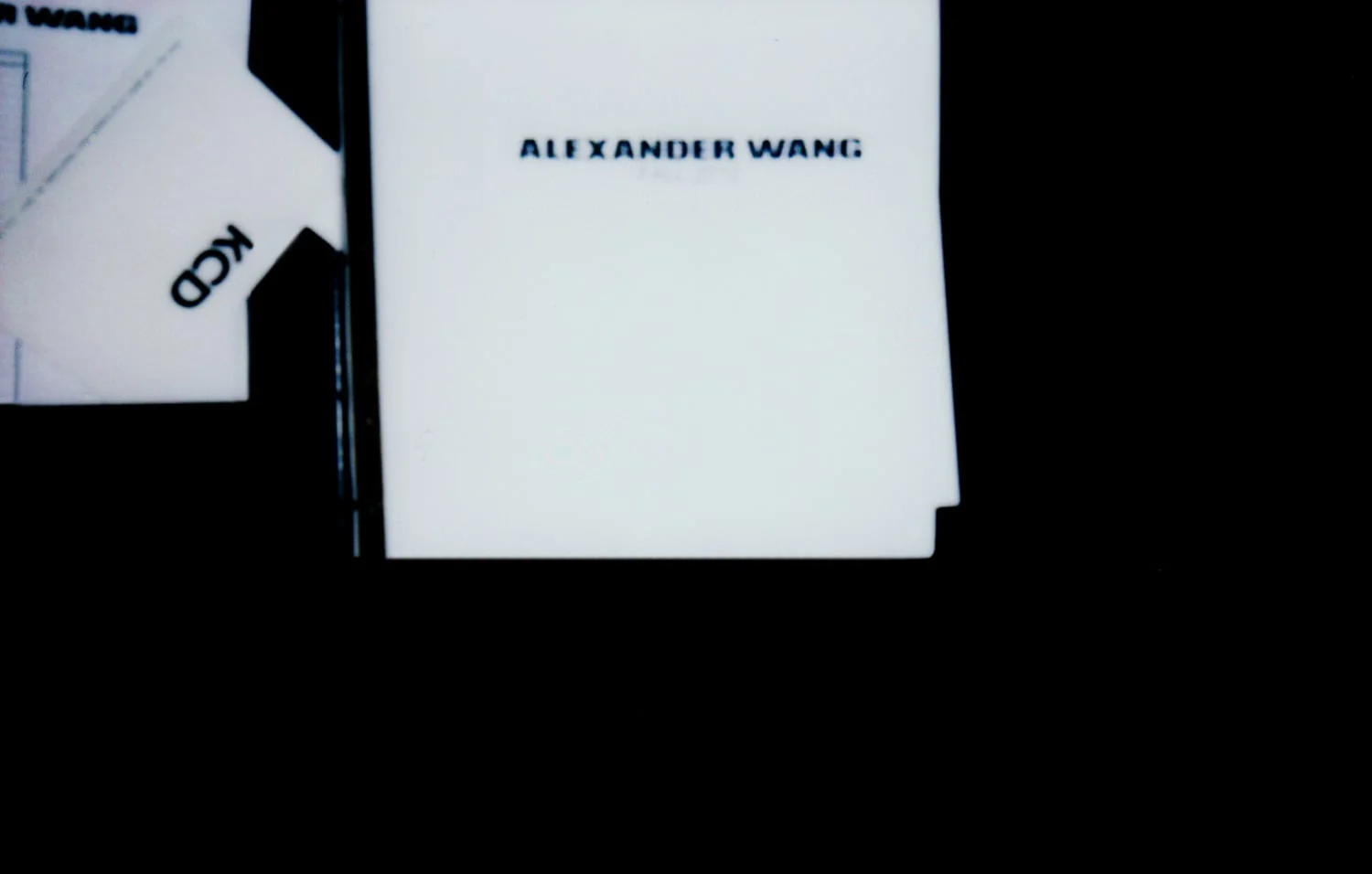 White Alexander Wang show invitation and a KCD card against a black background, for The New York Times Style Magazine.