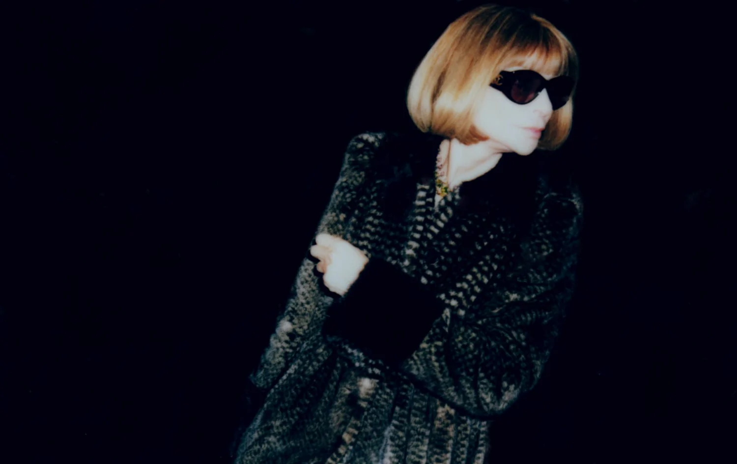 Woman with a blonde bob and dark sunglasses in a patterned fur coat on black, for The New York Times Style Magazine. Photographed by Cameron Krone.