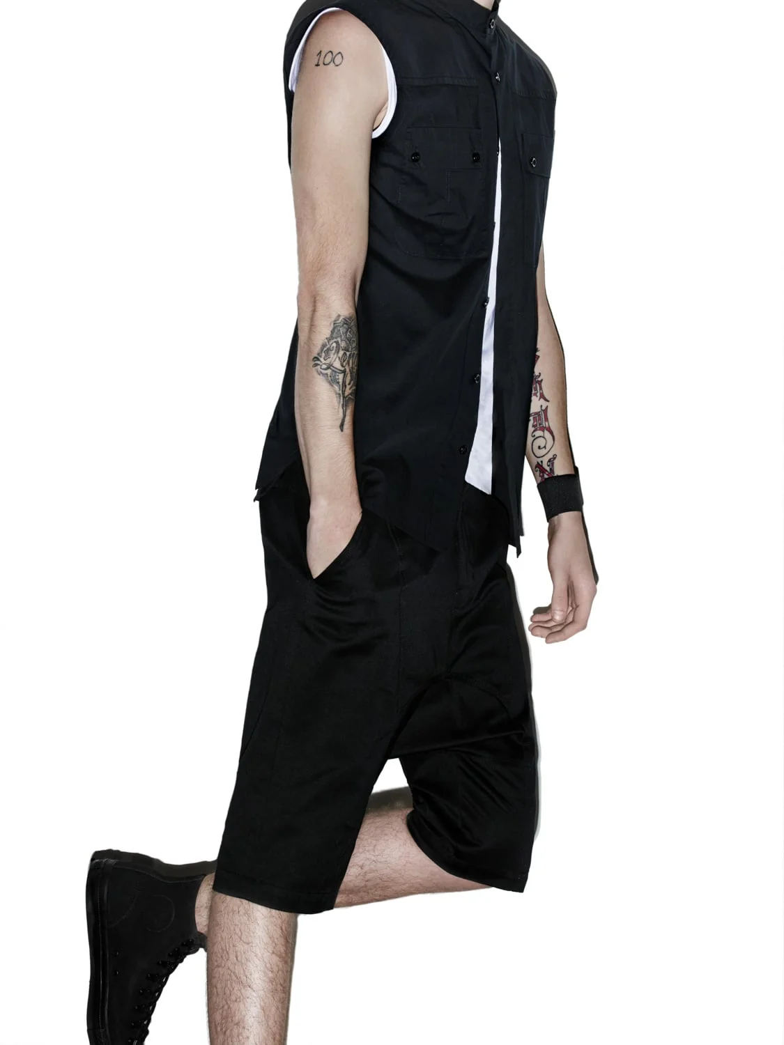 Tattooed model in a sleeveless black shirt, black shorts and high-top sneakers mid-stride on white, for Helmut Lang.