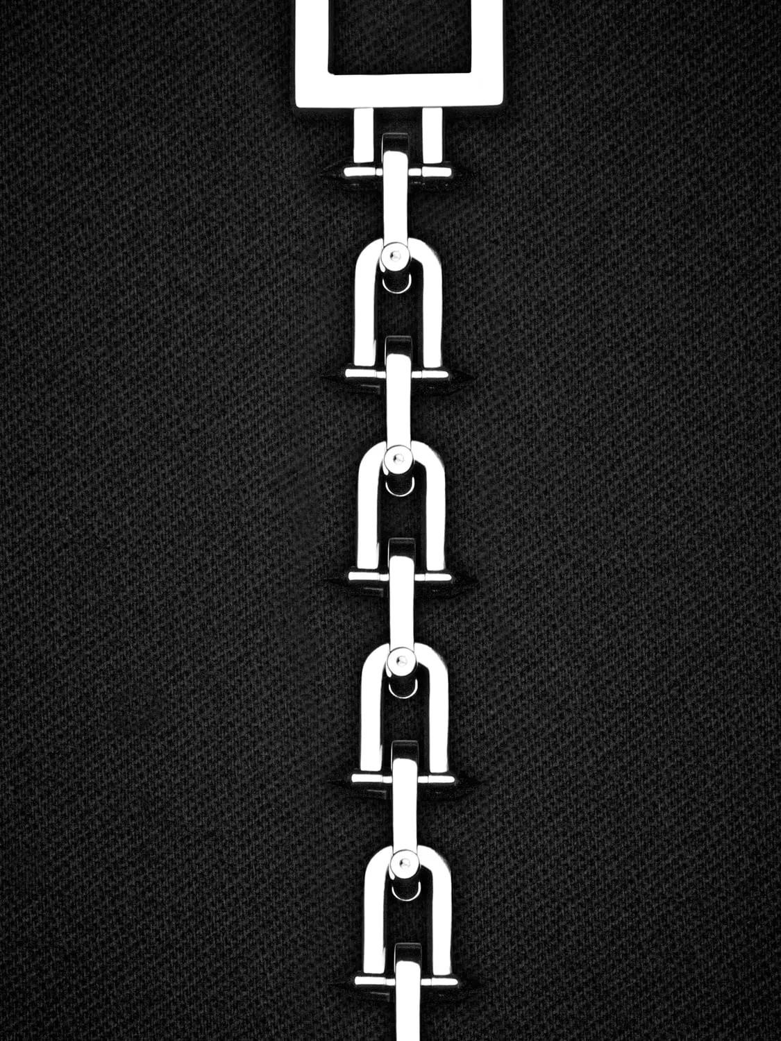 Polished silver chain of horseshoe-shaped links hanging vertically from a square link against dark woven fabric.