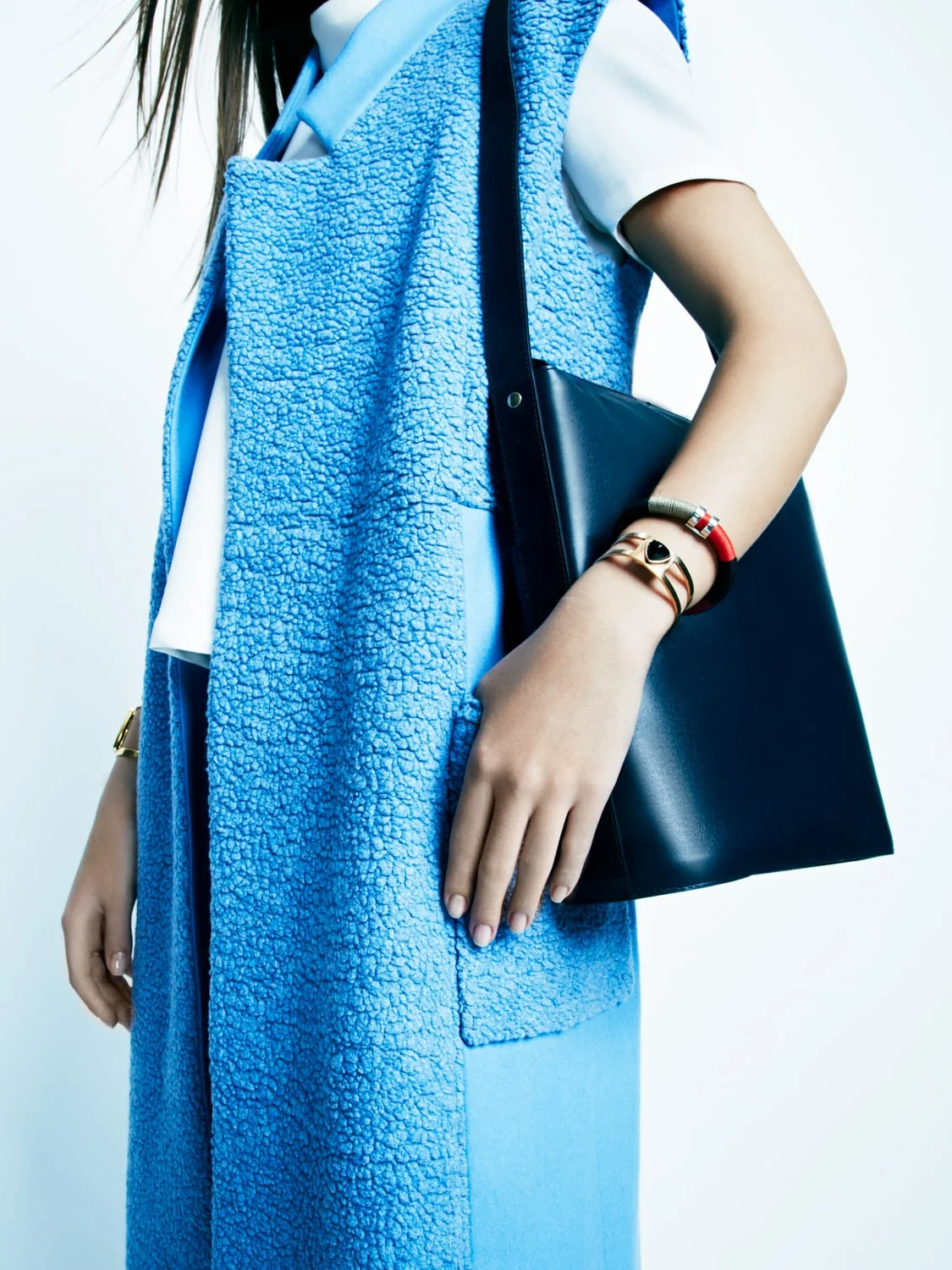Model in a sleeveless blue shearling coat with a navy leather shoulder bag and gold and red bracelets, for InStyle.