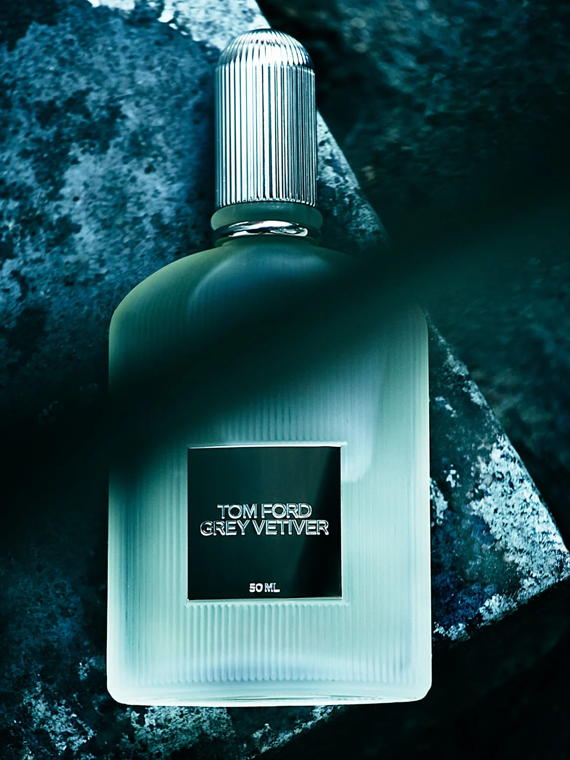 Frosted Grey Vetiver 50 ml perfume bottle with ribbed silver cap resting on dark blue-grey stone, for Tom Ford.