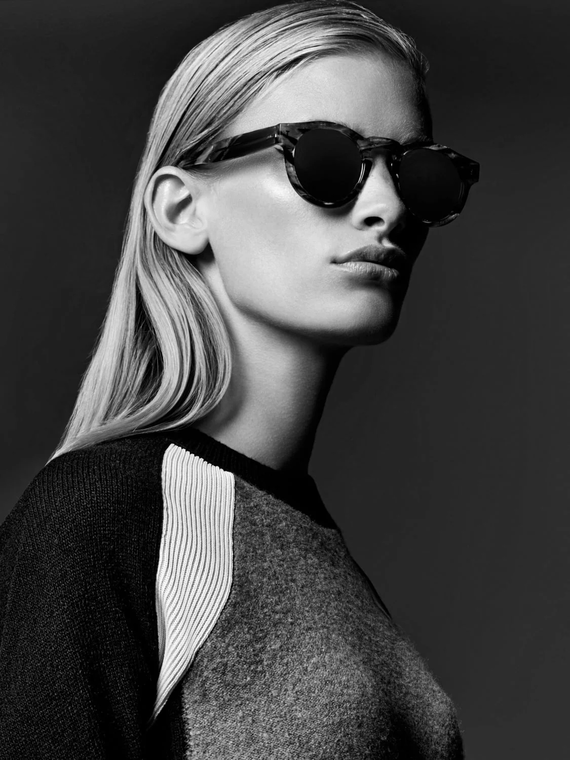 Black and white portrait of a blonde model in round tortoiseshell sunglasses and a colour-block knit sweater, for Saks Fifth Avenue.