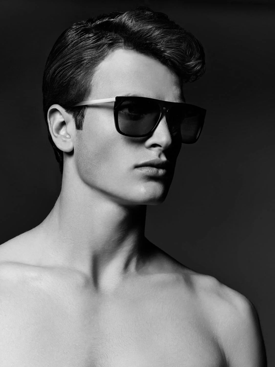 Black and white portrait of a shirtless man with swept-back hair wearing dark square sunglasses, for Saks Fifth Avenue.