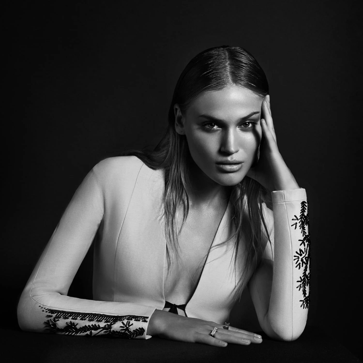 Black and white portrait of Sonya Gorelova in a white jacket with beaded cuffs, head resting on her hand against black. Photographed by Cameron Krone.