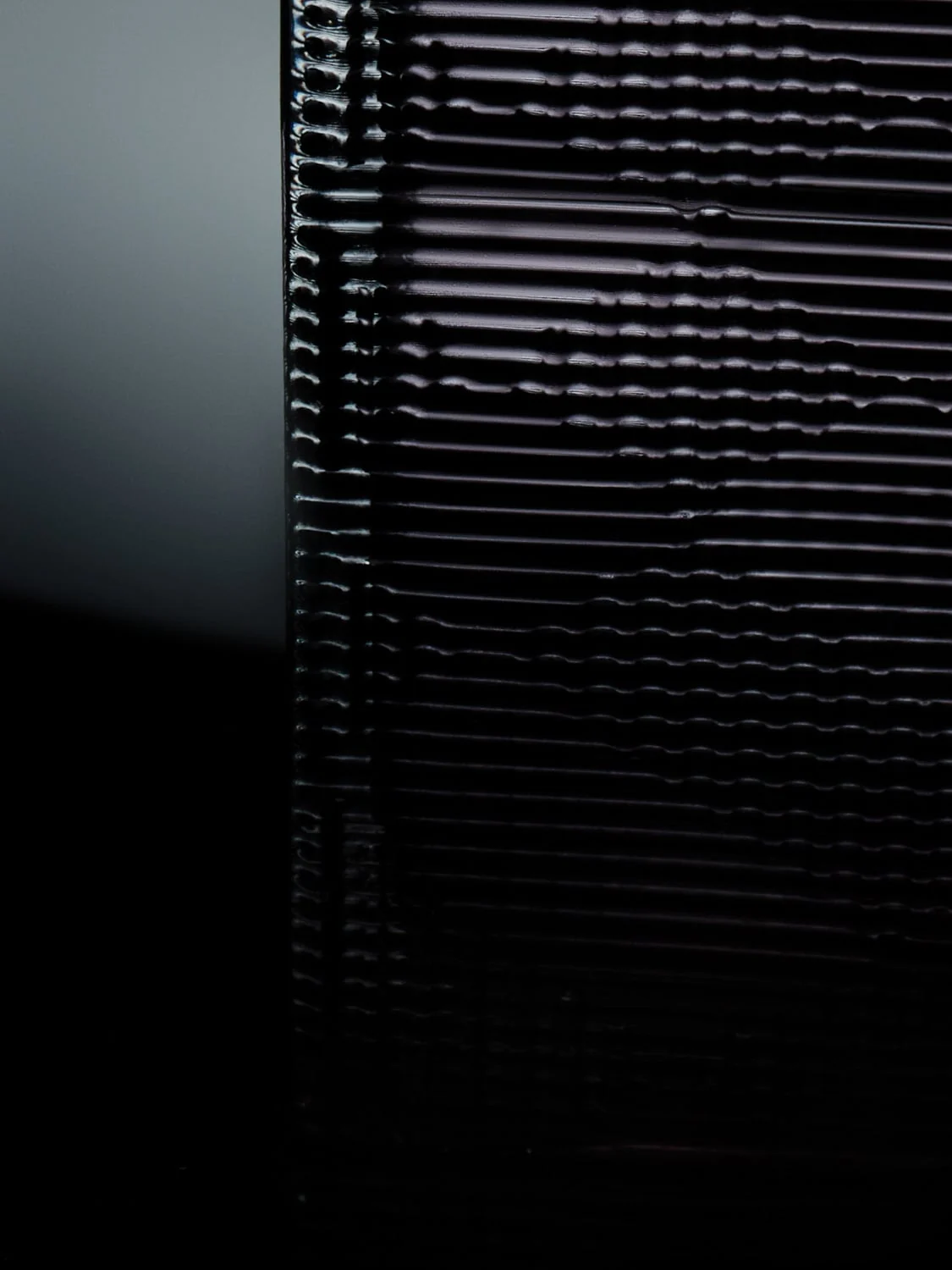 Close-up of a glossy black ribbed surface catching soft light against a grey and black background, for Burberry.