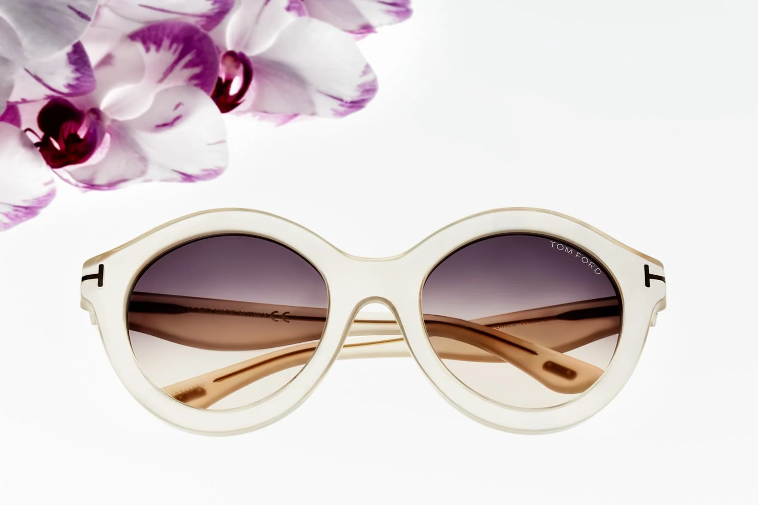 Ivory round sunglasses with gradient lenses beneath pink and white orchids on a white background, for Tom Ford. Photographed by Cameron Krone.
