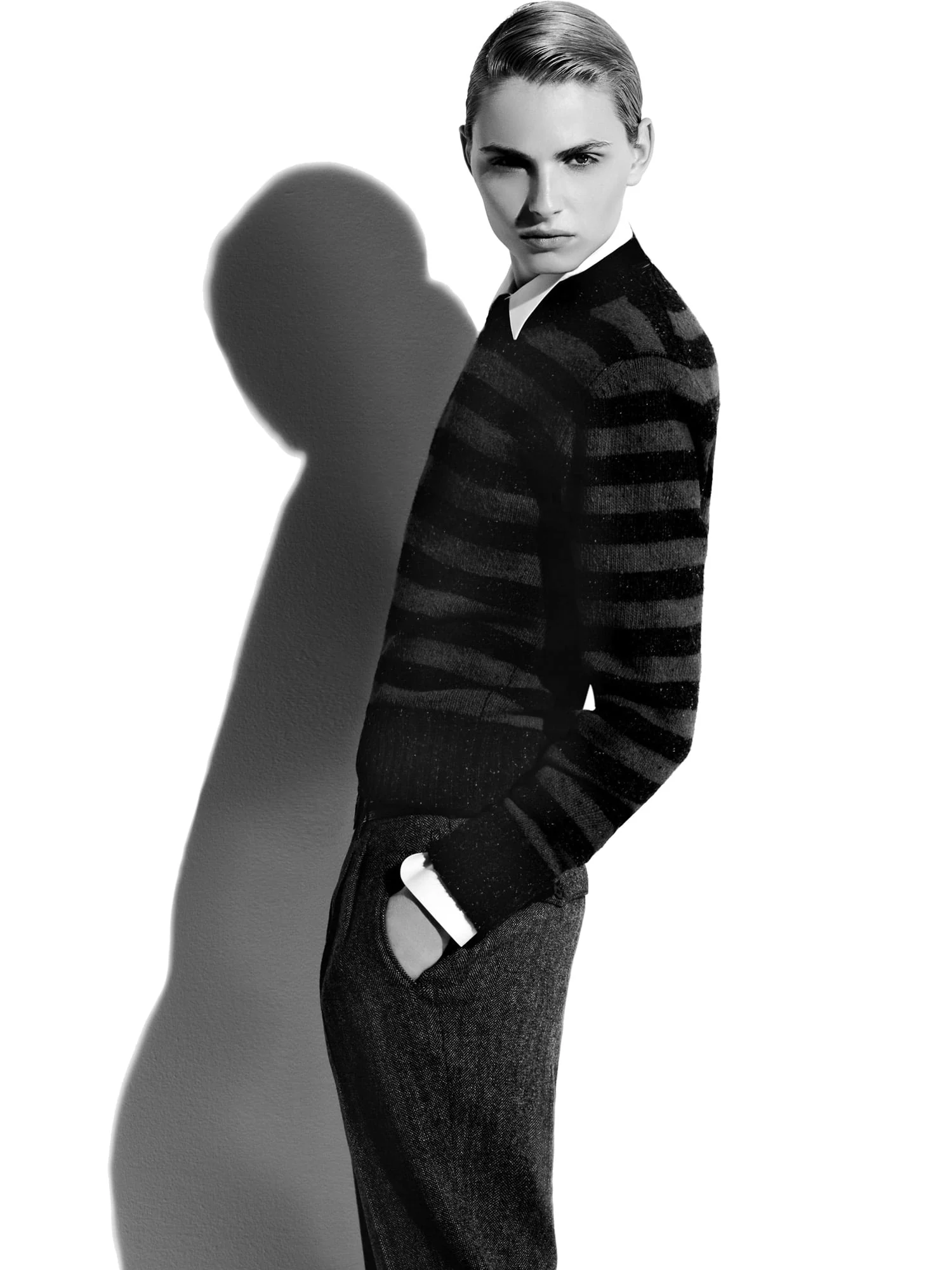 Black and white shot of a model in a striped sweater and tweed trousers, hand in pocket, casting a long shadow, for Apropos.