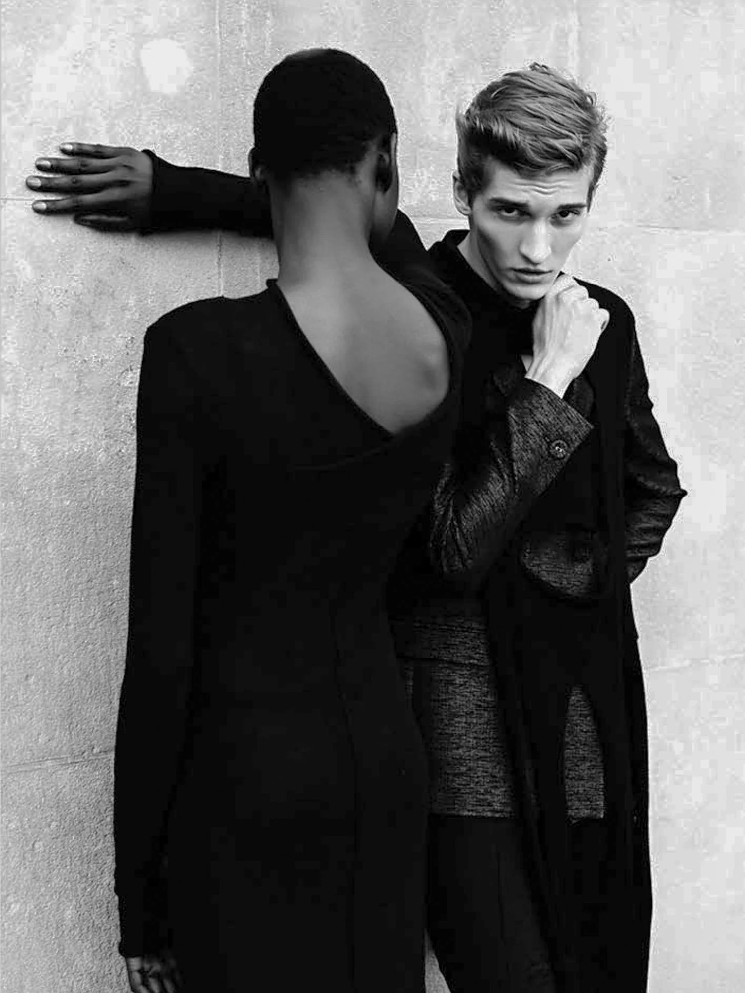 Black-and-white image of two models in black clothing against a stone wall, one facing away in a low-back dress, for Bon.