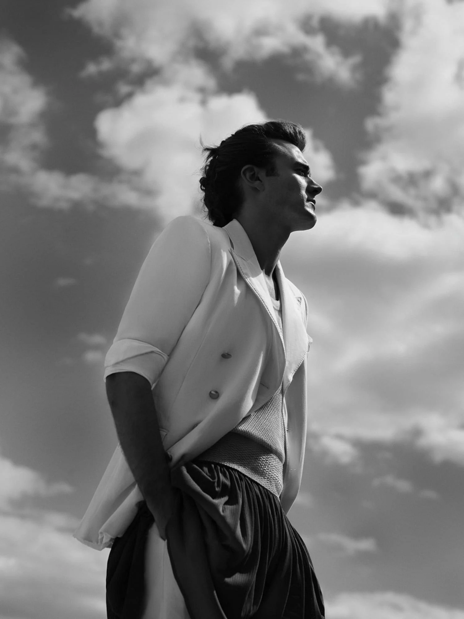 Black and white portrait of Brad Kroenig in a white double-breasted jacket, shot from below against a cloudy sky.