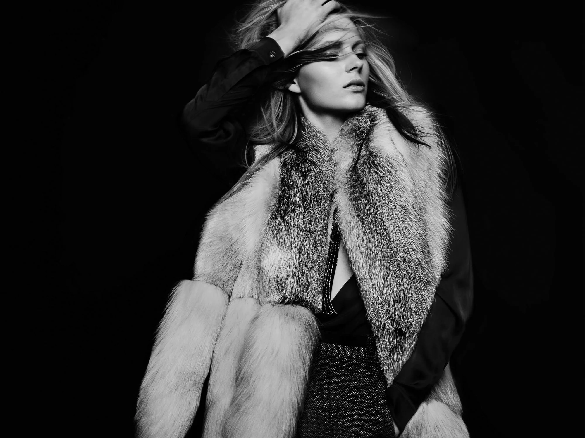 Black and white shot of a blonde model in a long fur stole and dark blouse, hand in her hair, for French Revue des Modes.