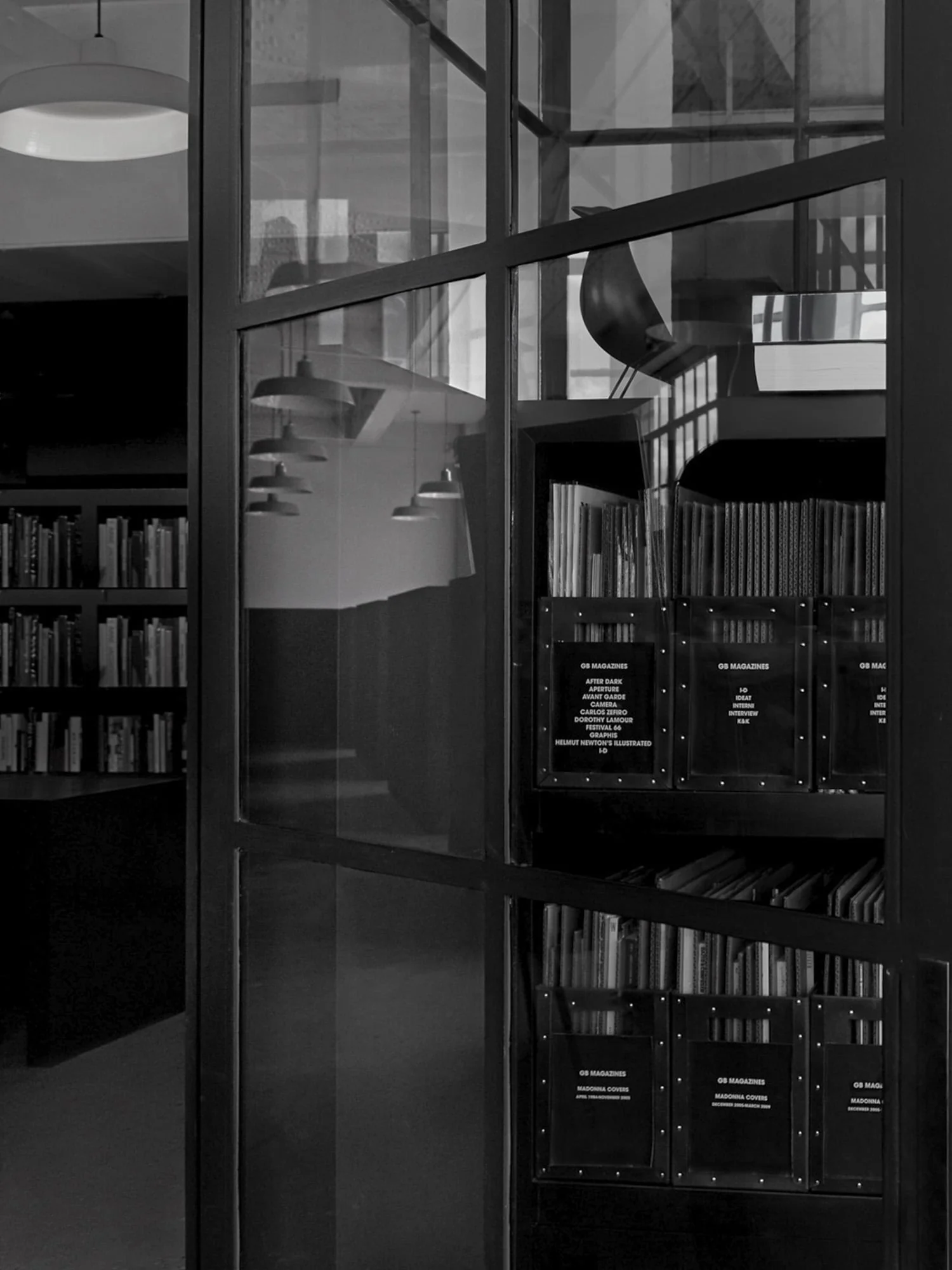 Black and white view through a steel-framed glass partition to shelves of labelled magazine archive boxes, for Giovanni Bianco.