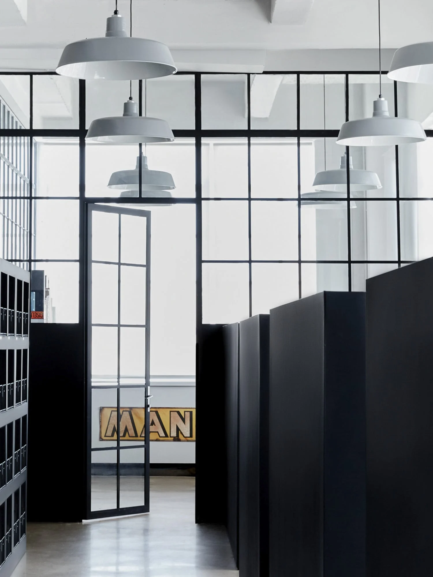 Studio interior with black steel-framed glass partition, white pendant lamps and black cabinets, for Giovanni Bianco.