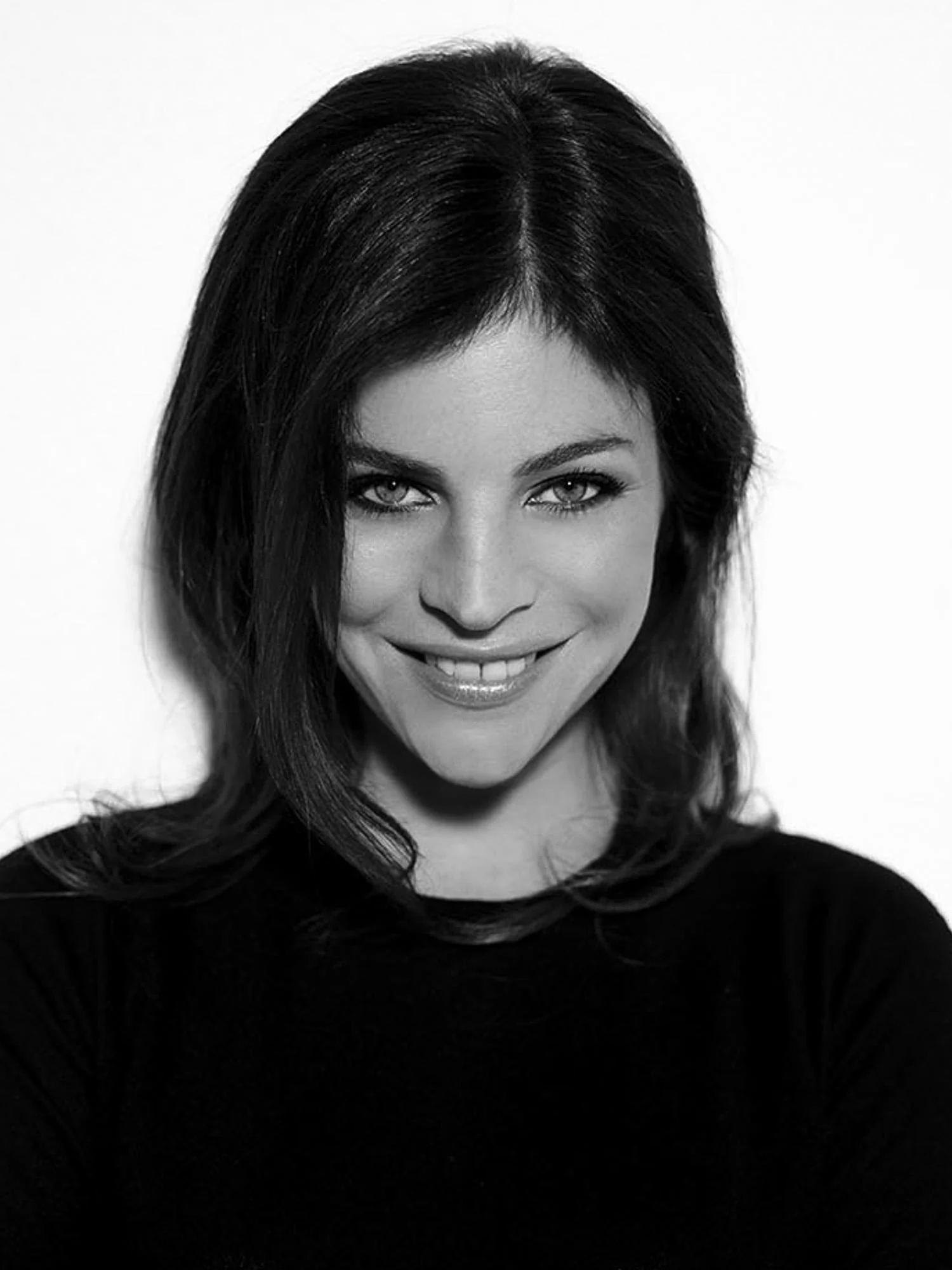 Black-and-white portrait of Julia Roitfeld smiling, with long dark hair and a black top against a white background.