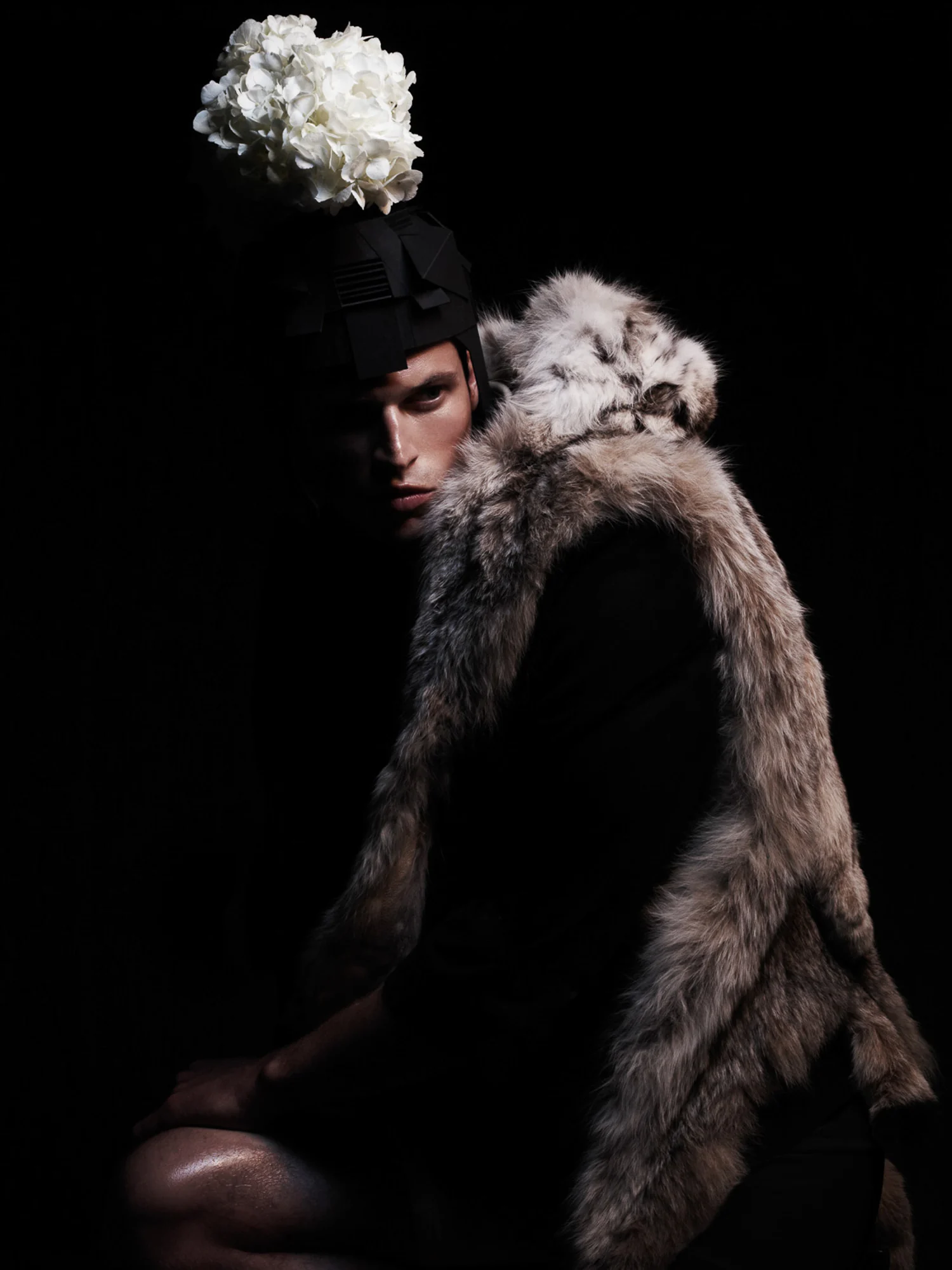 Lars Burmeister in a lynx fur stole and black headpiece topped with white hydrangeas against a dark background.