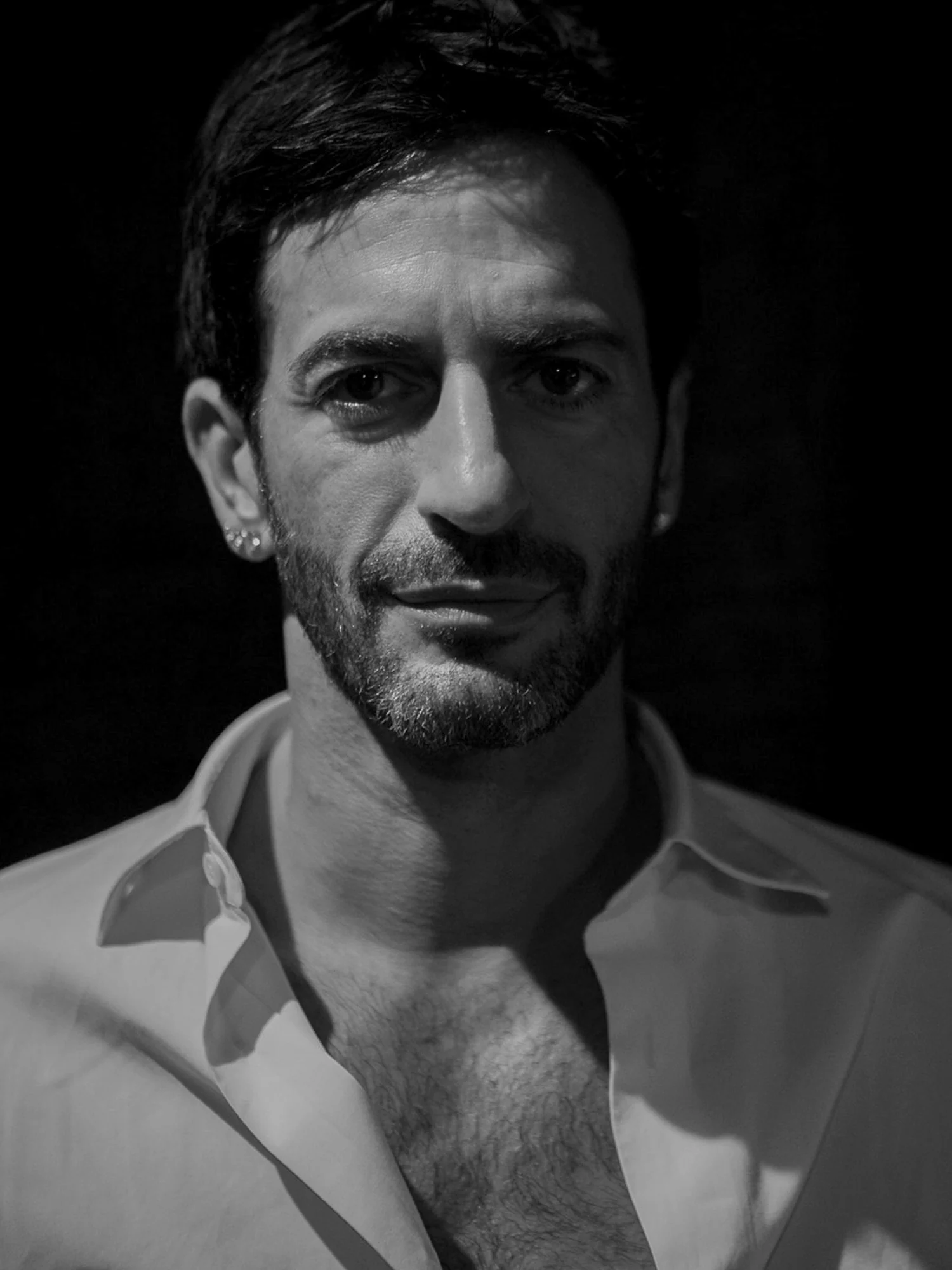 Black and white portrait of Marc Jacobs in an open-collared white shirt against a dark background.