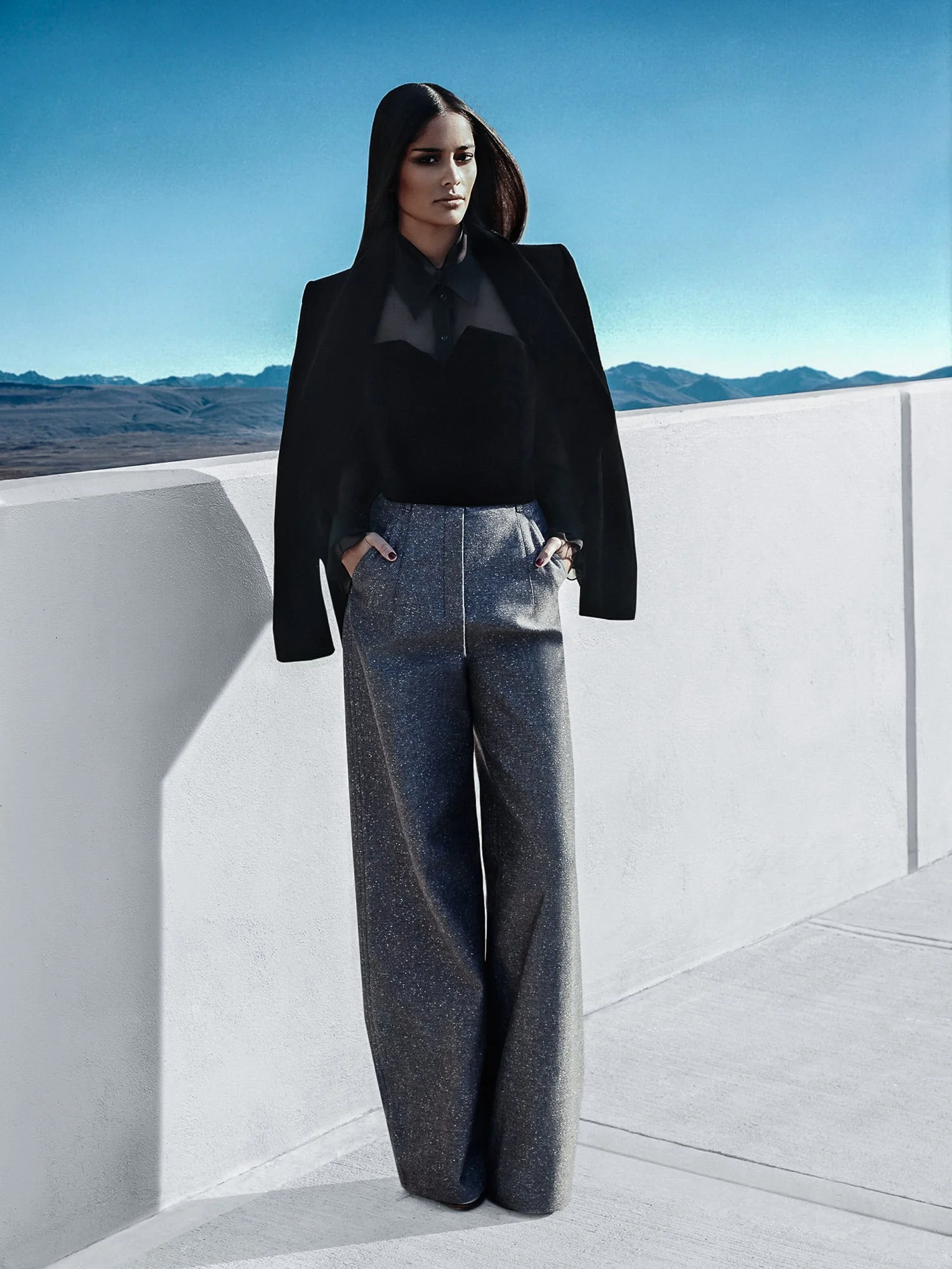 Model in black jacket, sheer black blouse and grey tweed wide-leg trousers on a white rooftop, for The New York Times. Photographed by Cameron Krone.