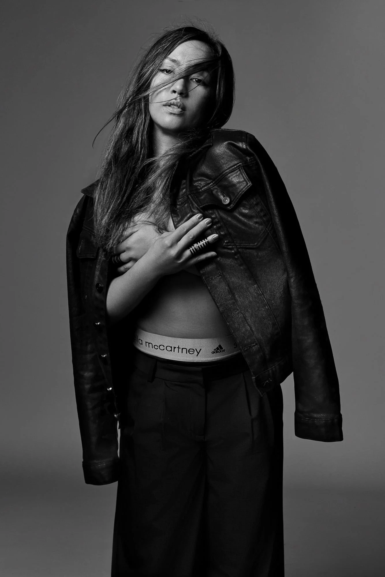 Black-and-white portrait of Nicole Winhoffer in a leather jacket draped over her shoulders, hair blowing, arms across her chest.