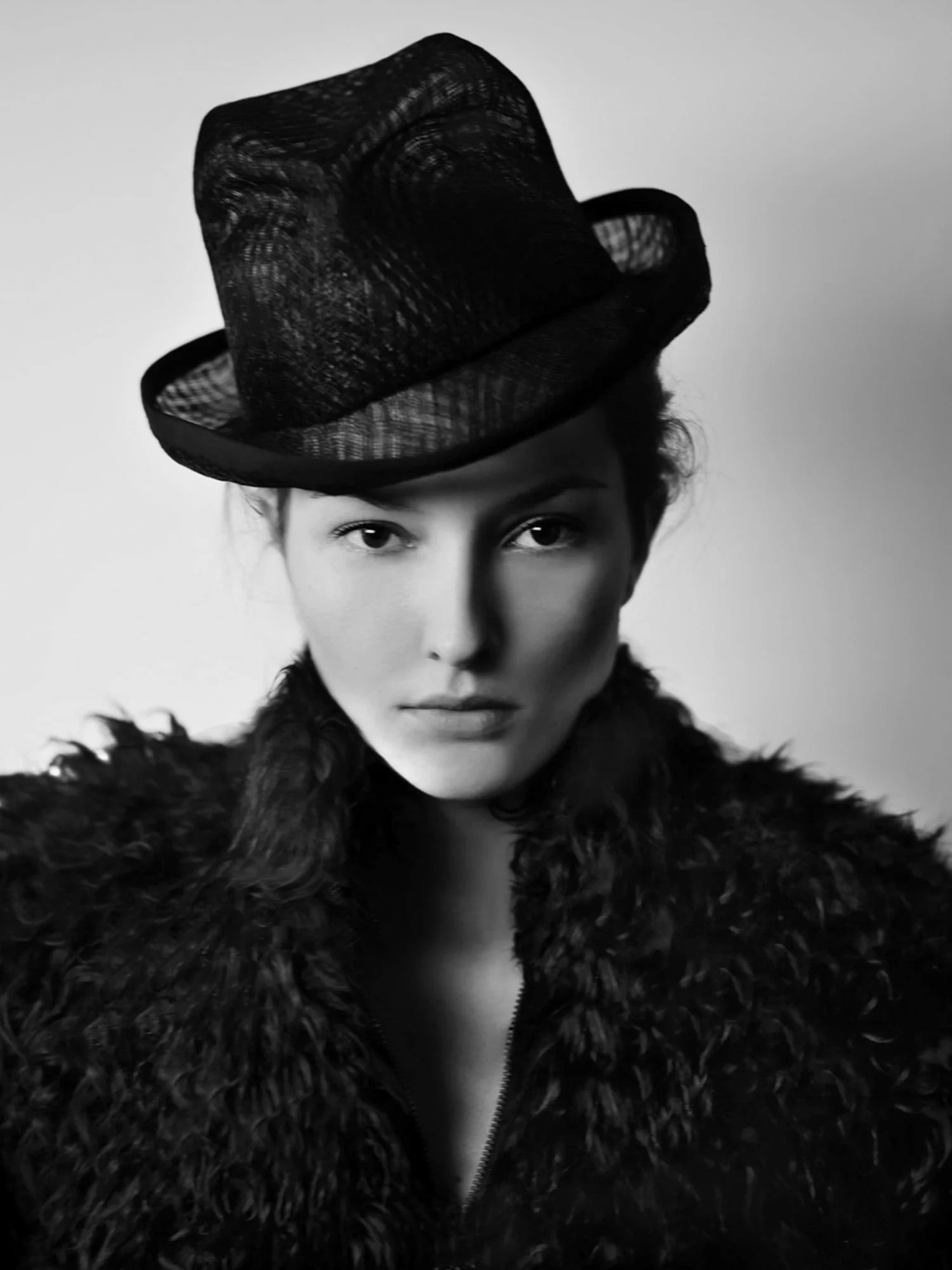 Black and white portrait of Solange Wilvert in a black mesh fedora and shaggy fur coat against a pale wall.