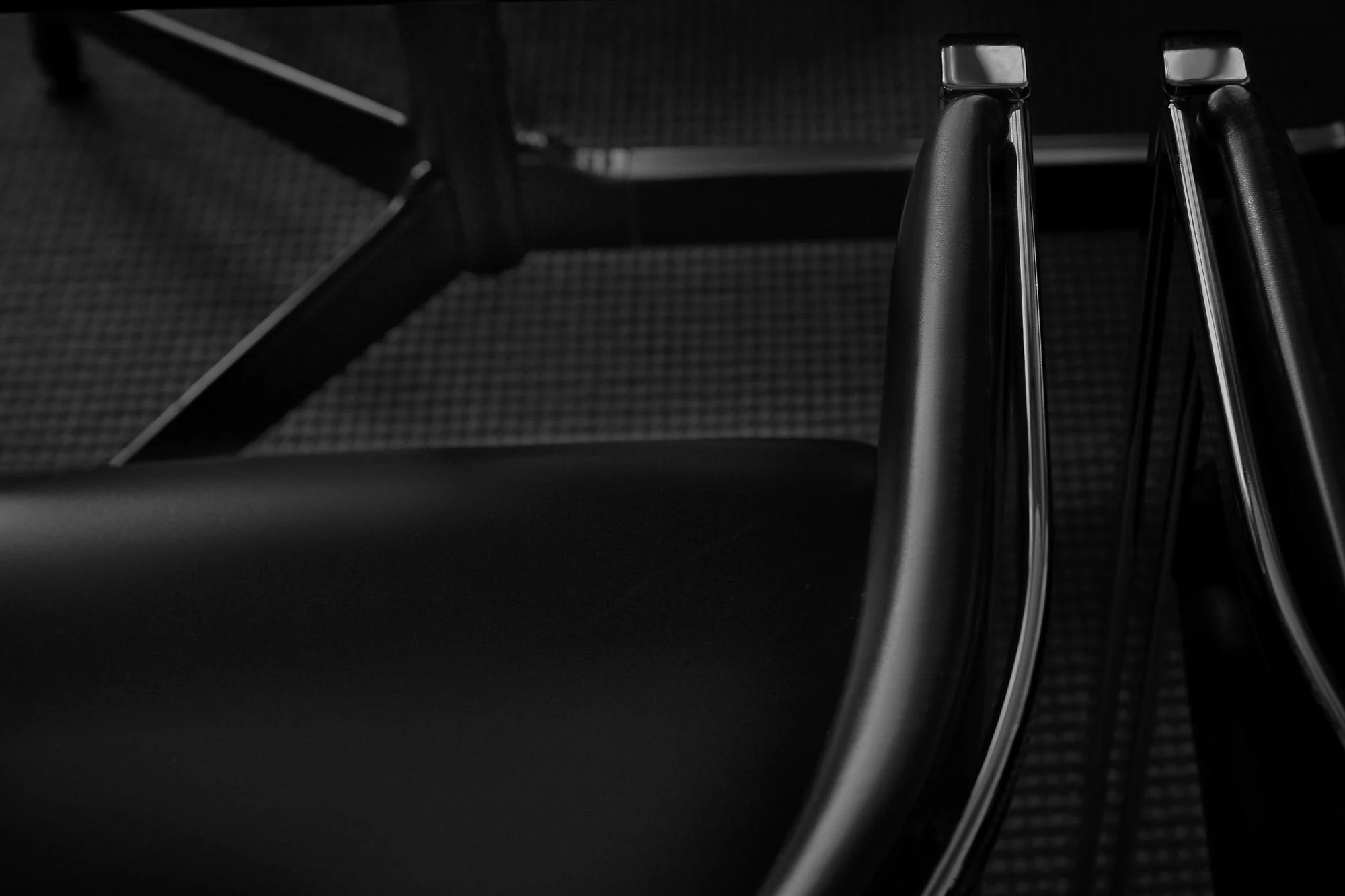 Close-up of a black leather chair seat and chrome-edged armrests over a dark woven carpet, for Viana Art.
