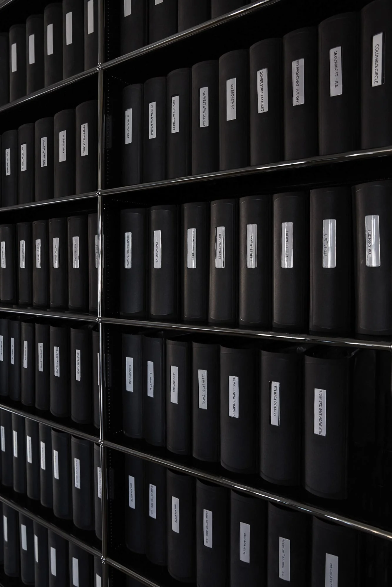 Rows of black archive binders with white spine labels on chrome shelving in a dim room, for Viana Art.