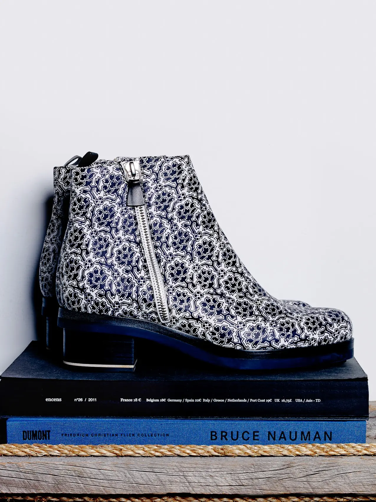 Navy and white patterned ankle boots with silver side zips, posed on stacked books atop a rope-trimmed wooden shelf, for Elle.