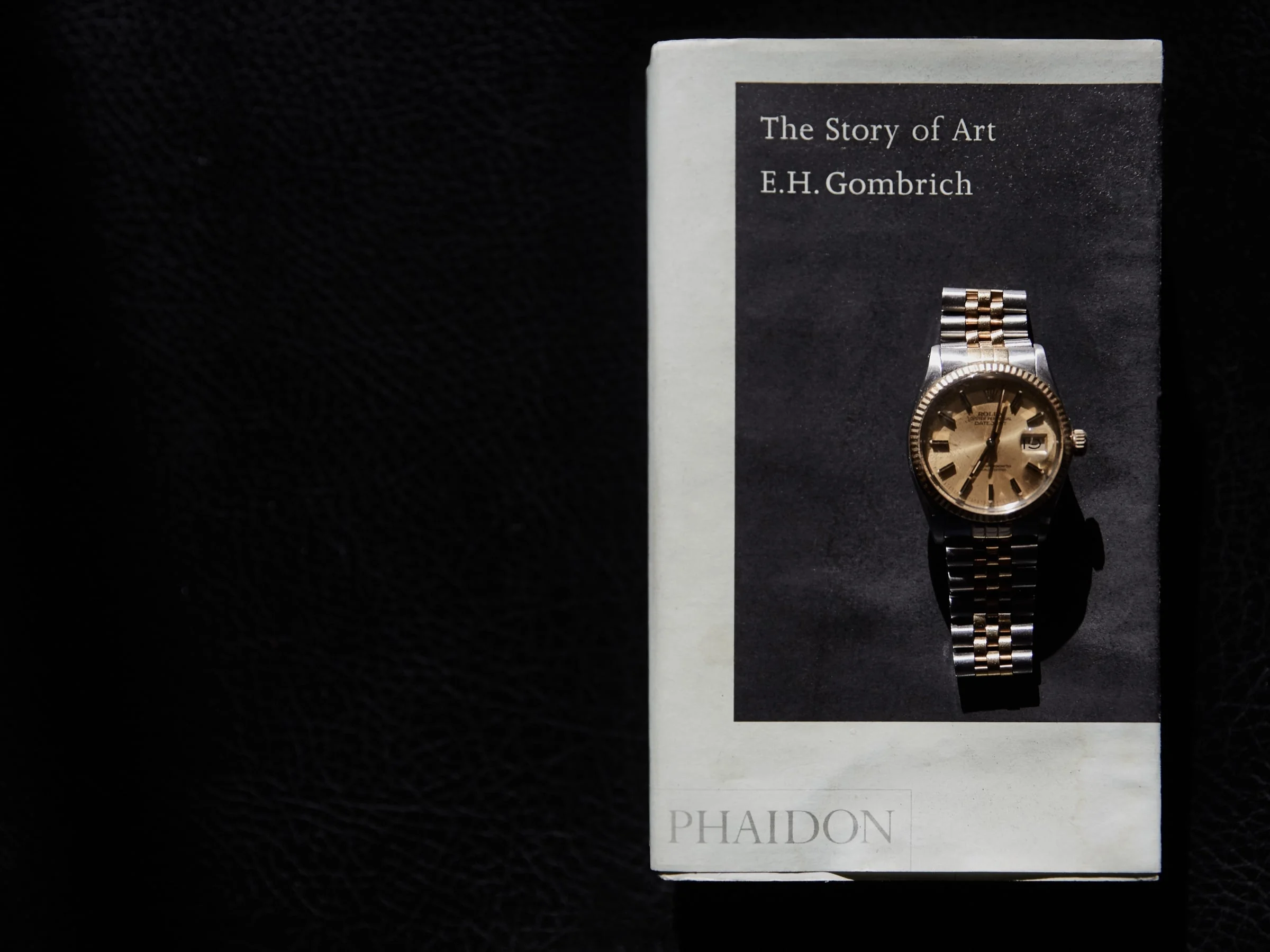 Two-tone gold and steel wristwatch resting on a copy of The Story of Art by E.H. Gombrich on black leather.