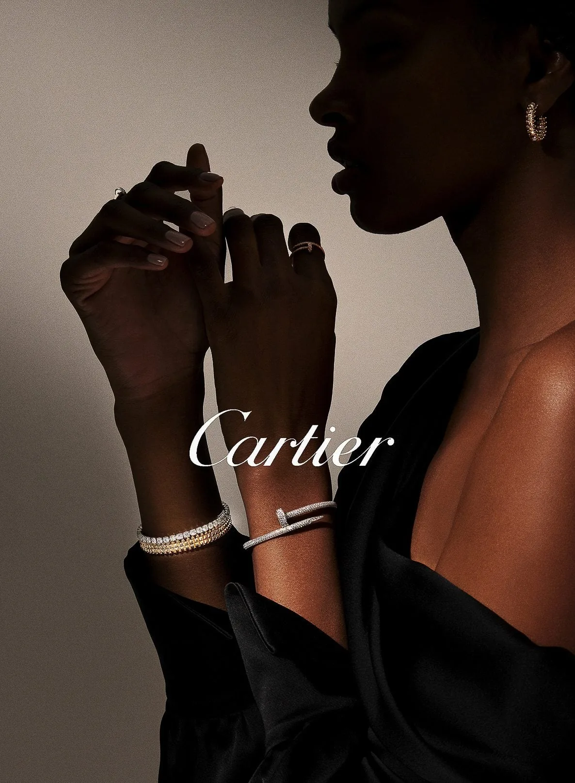 Model in profile wearing a black satin top, diamond bangles, a Juste un Clou bracelet and hoop earrings, for Cartier.