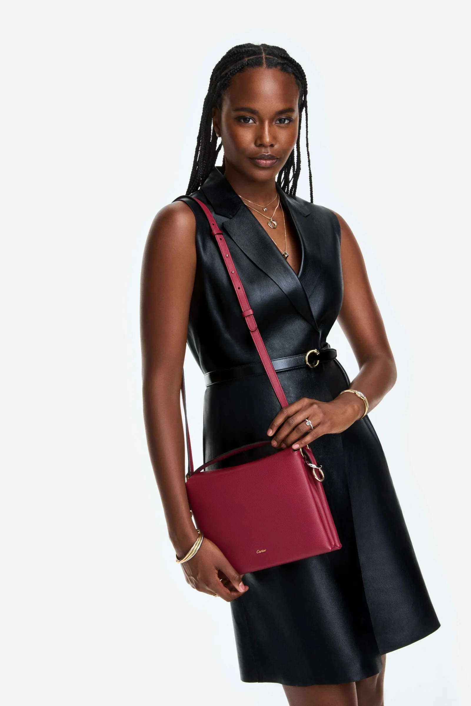 Model in a black leather sleeveless dress carrying a crimson leather crossbody bag against a white backdrop, for Cartier.