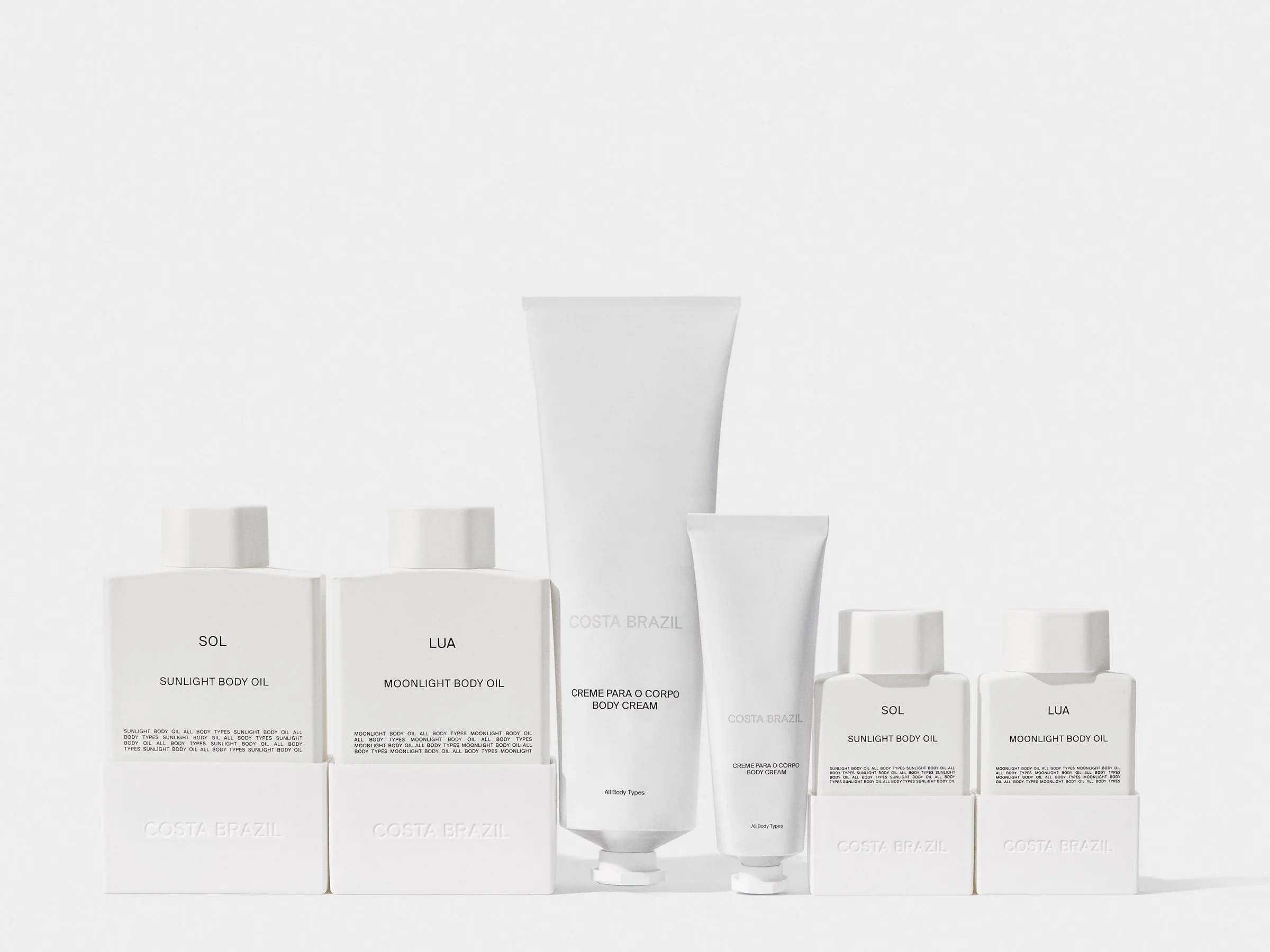 Still life of white Sol and Lua body oil bottles and body cream tubes lined up on a pale grey backdrop, for Costa Brazil.