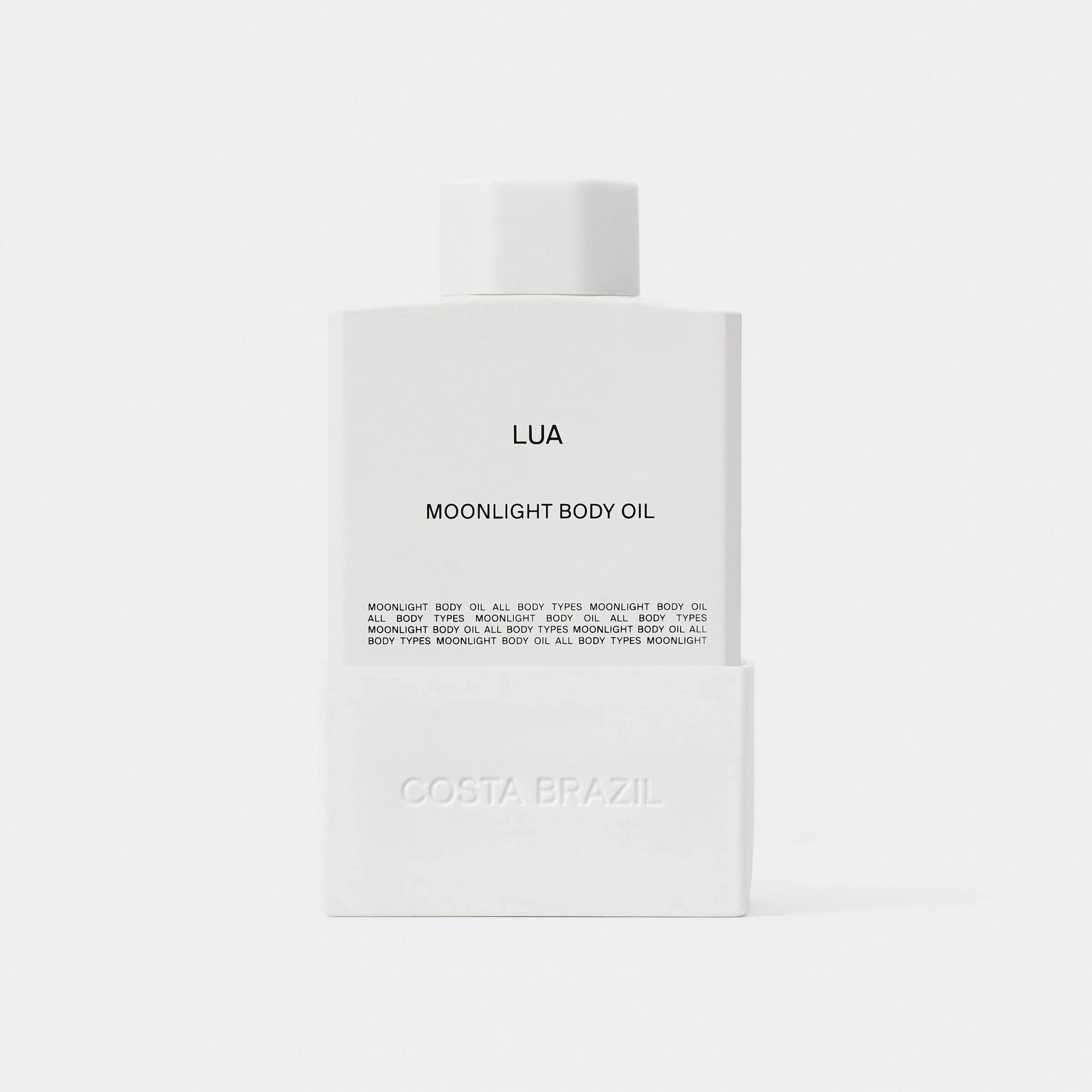 White Lua Moonlight Body Oil bottle with embossed sleeve, a still life on a pale grey backdrop, for Costa Brazil.