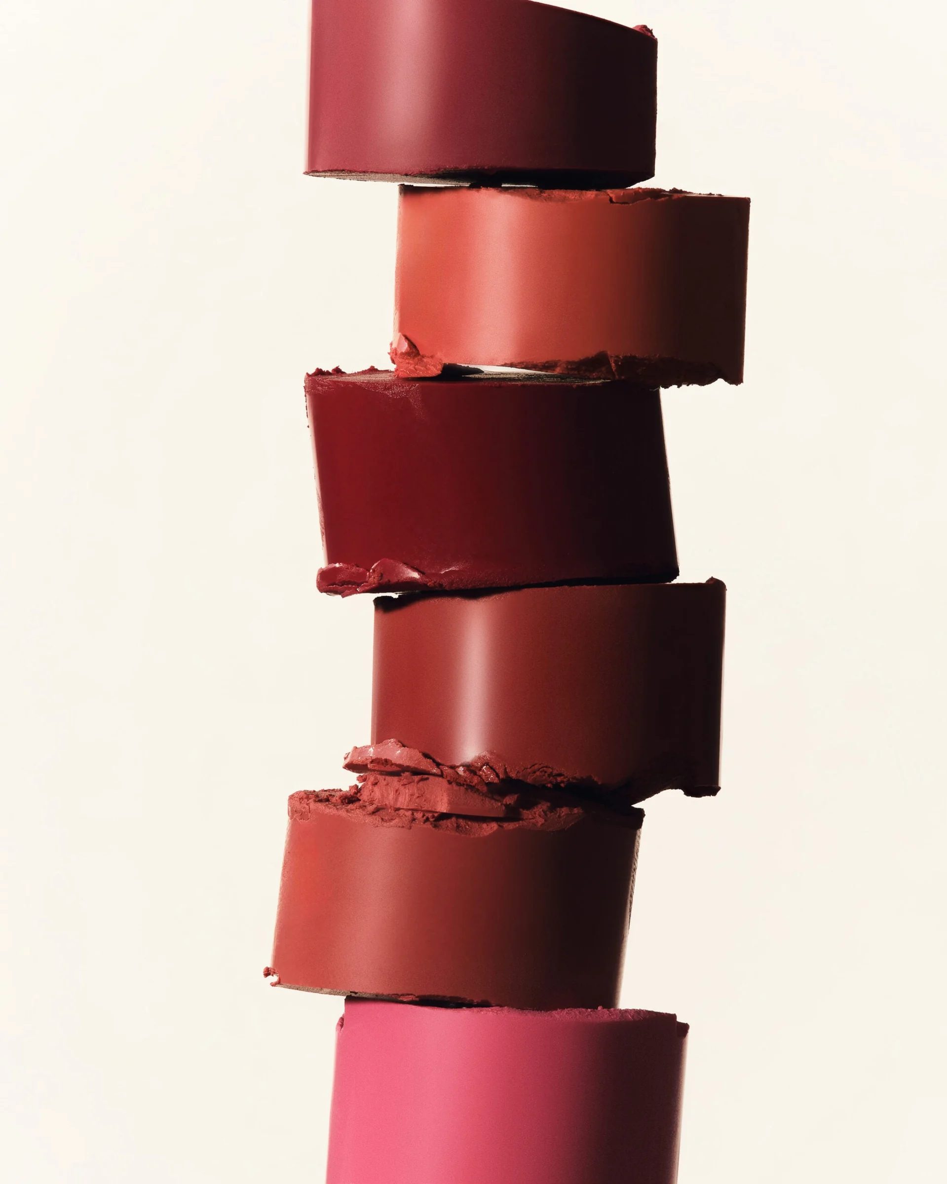 Stack of cut lipstick bullets in red, coral, berry and pink shades on a cream background, for Kylie Cosmetics.