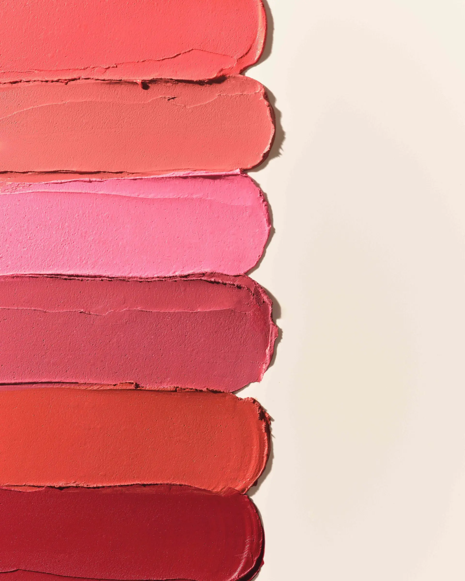 Six lipstick swatches in coral, pink, rose, orange and red smeared across a cream background, for Kylie Cosmetics.