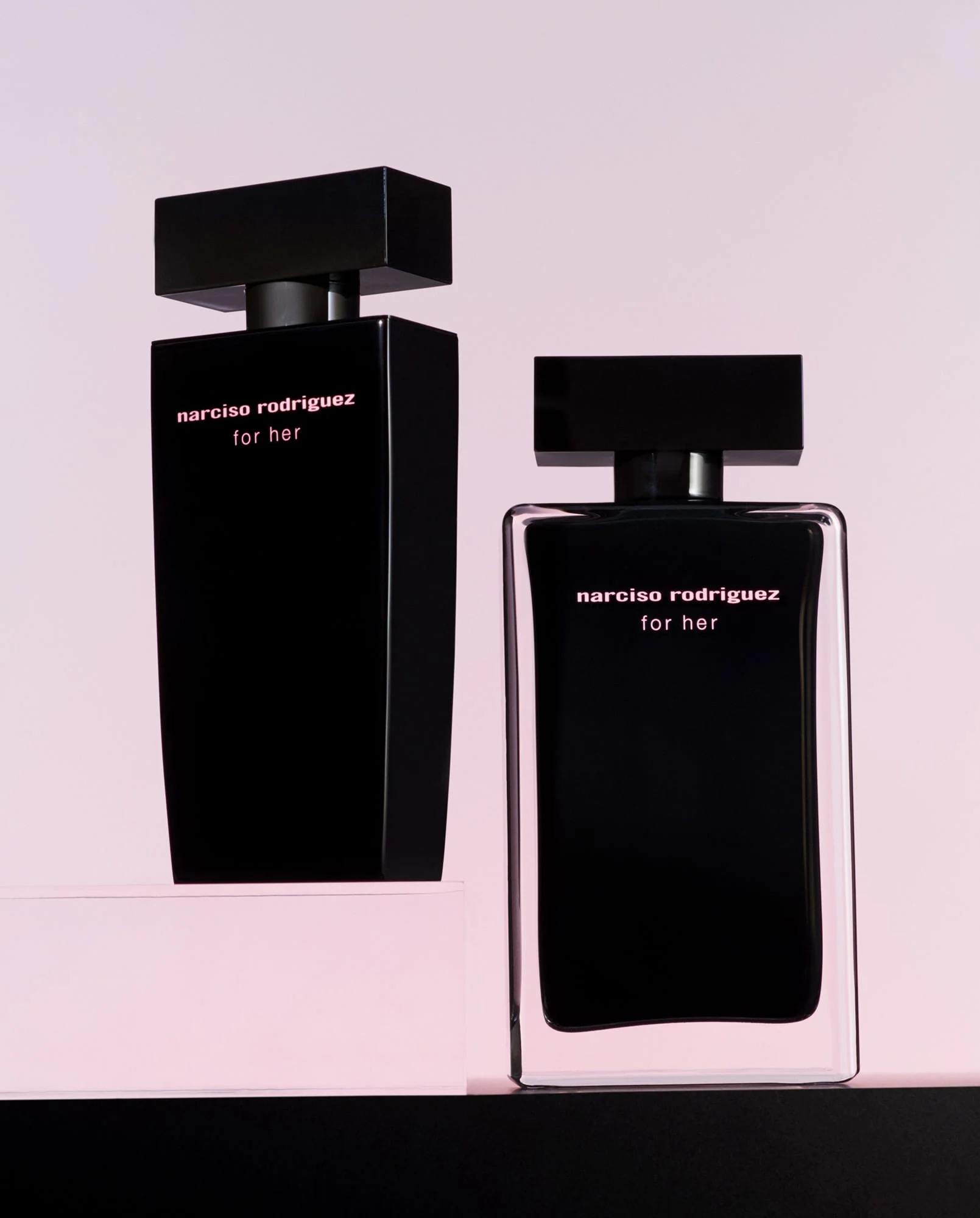 Two black For Her fragrance bottles on pink and black plinths against a soft pink backdrop, for Narciso Rodriguez.